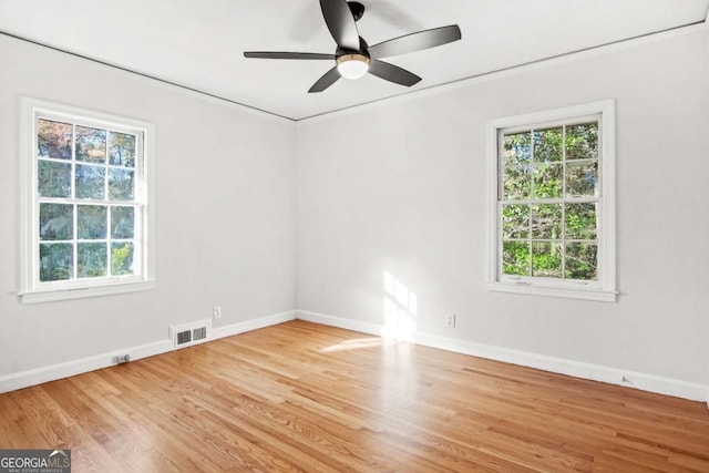 spare room with a wealth of natural light, visible vents, baseboards, and wood finished floors