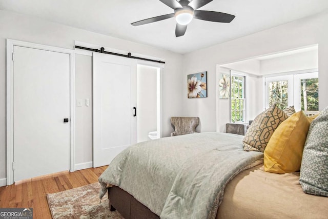 bedroom with ceiling fan, a barn door, and light wood-style flooring