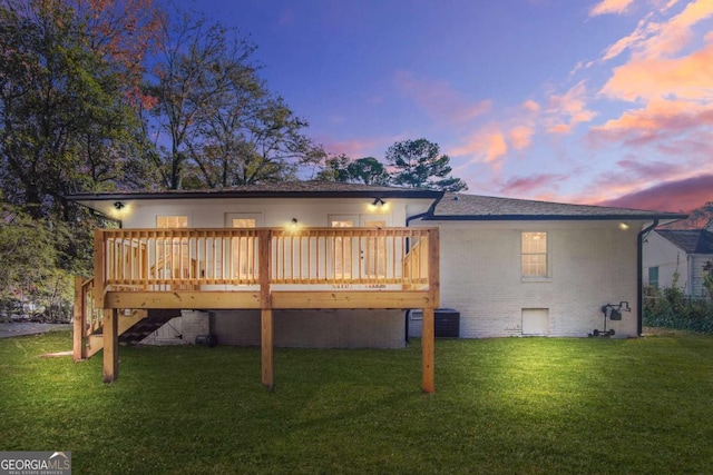 back of house at dusk with stairway, a deck, central air condition unit, a lawn, and brick siding