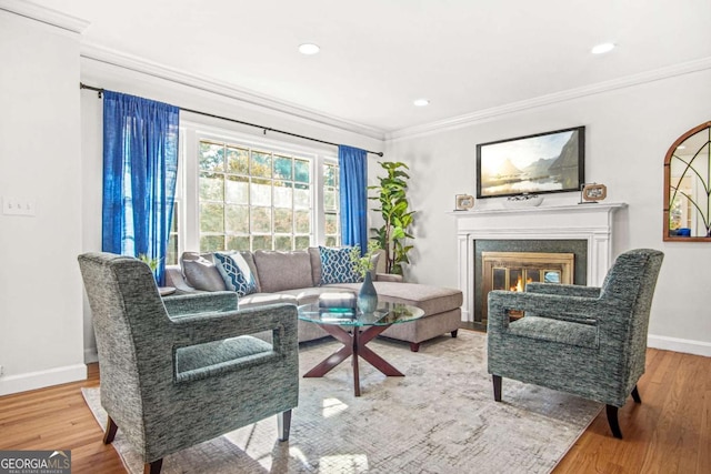 living room featuring a glass covered fireplace, ornamental molding, baseboards, and wood finished floors