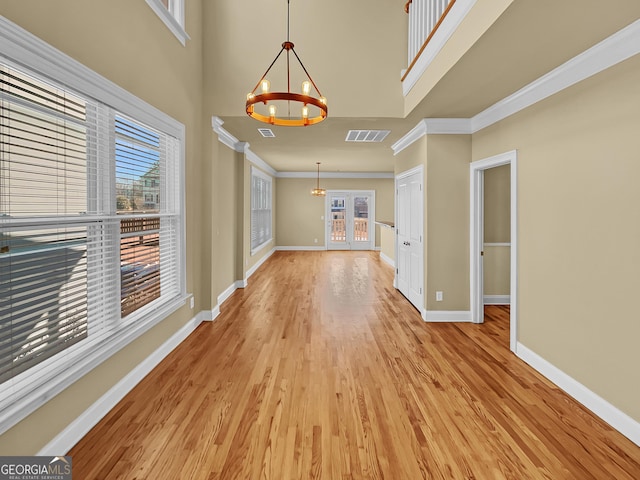 interior space with baseboards, visible vents, light wood finished floors, an inviting chandelier, and ornamental molding