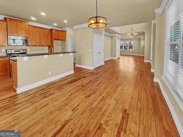 kitchen featuring dark countertops, open floor plan, light wood-style flooring, stainless steel appliances, and a kitchen island with sink