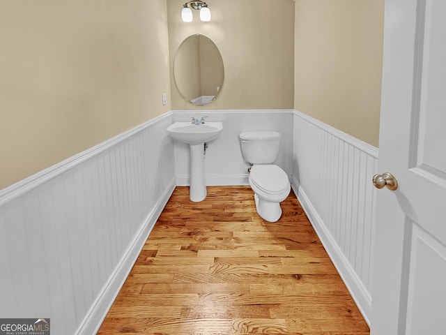 half bath featuring toilet, wood finished floors, and wainscoting