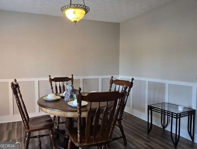 dining space with a decorative wall, wainscoting, and dark wood-type flooring