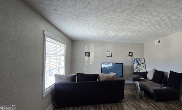 living area featuring plenty of natural light, wood finished floors, visible vents, and a textured wall