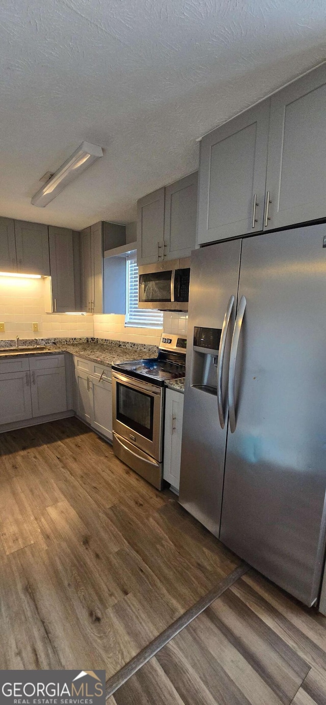 kitchen featuring dark wood-style flooring, gray cabinetry, appliances with stainless steel finishes, a textured ceiling, and tasteful backsplash