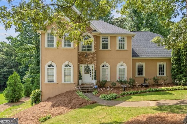 colonial inspired home with stucco siding, stone siding, and a shingled roof