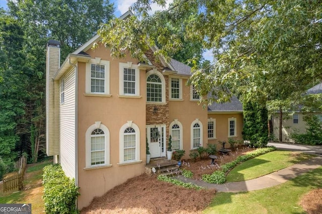 colonial inspired home with a shingled roof, stucco siding, and a chimney