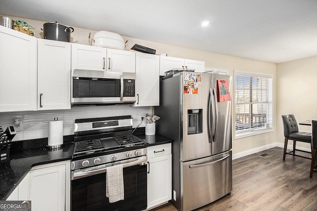 kitchen featuring dark countertops, tasteful backsplash, appliances with stainless steel finishes, white cabinets, and dark wood-style flooring