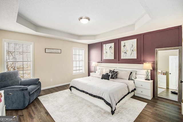 bedroom featuring dark wood finished floors, a tray ceiling, baseboards, and a textured ceiling