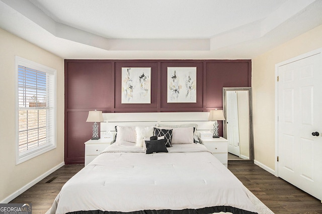 bedroom with baseboards, a raised ceiling, visible vents, and dark wood finished floors