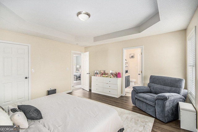 bedroom with a raised ceiling, dark wood-style floors, and connected bathroom