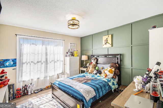 bedroom with a decorative wall, wood finished floors, and a textured ceiling