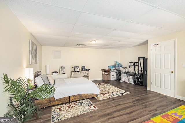 bedroom featuring a drop ceiling, baseboards, visible vents, and wood finished floors