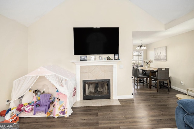 living area with lofted ceiling, wood finished floors, an inviting chandelier, baseboards, and a tile fireplace