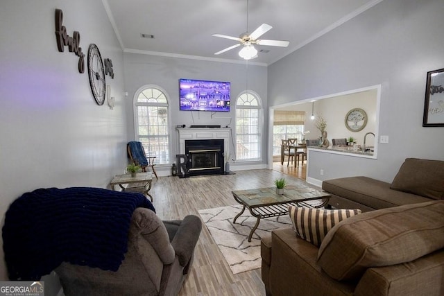 living room featuring visible vents, ornamental molding, a ceiling fan, a glass covered fireplace, and wood finished floors