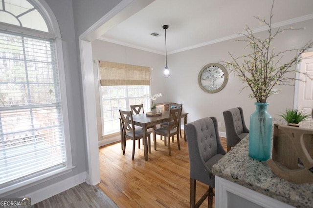 dining area featuring visible vents, baseboards, crown molding, and light wood finished floors