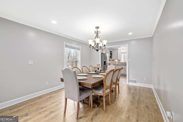 dining area featuring visible vents, light wood-type flooring, crown molding, and baseboards