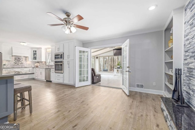 living area with visible vents, a ceiling fan, crown molding, and light wood finished floors