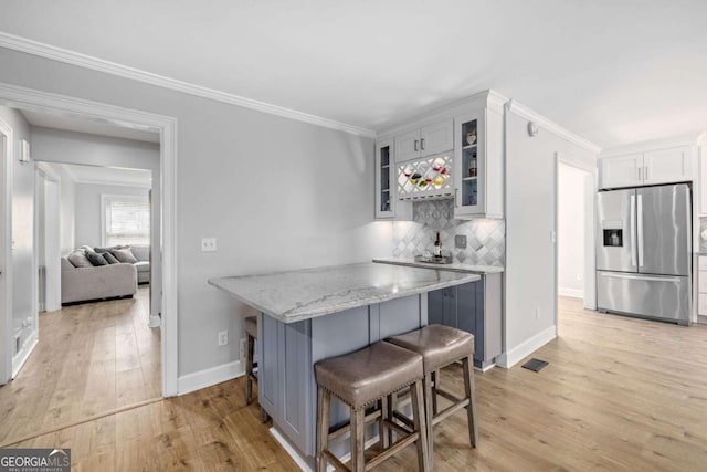 kitchen with tasteful backsplash, glass insert cabinets, light wood-type flooring, a kitchen breakfast bar, and stainless steel fridge