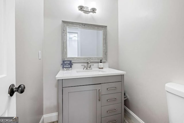 half bathroom with vanity, toilet, and baseboards