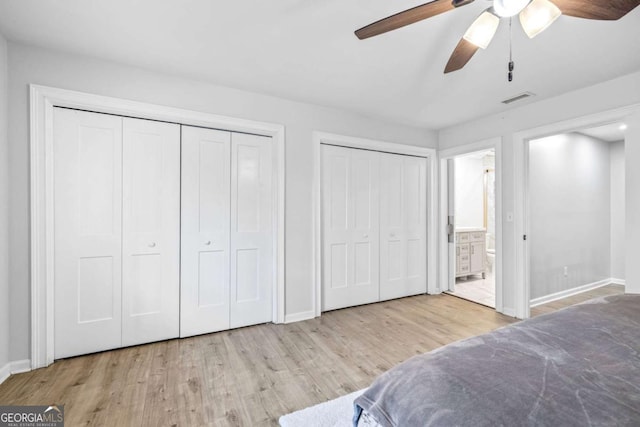 bedroom featuring visible vents, multiple closets, baseboards, and wood finished floors