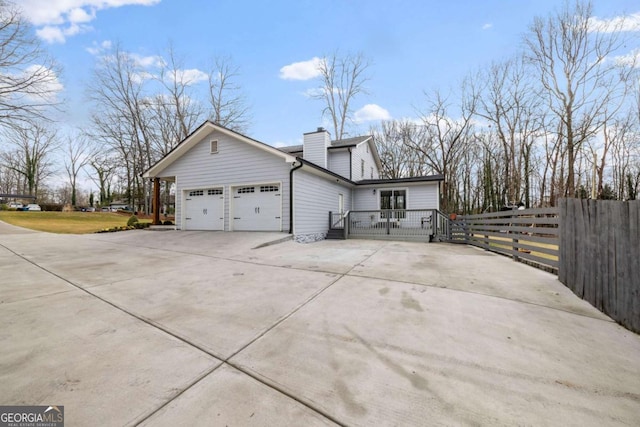 view of home's exterior with an attached garage, a chimney, driveway, and fence