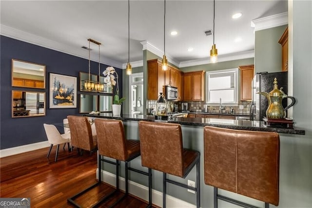 kitchen featuring a peninsula, dark wood-style flooring, stainless steel appliances, hanging light fixtures, and tasteful backsplash