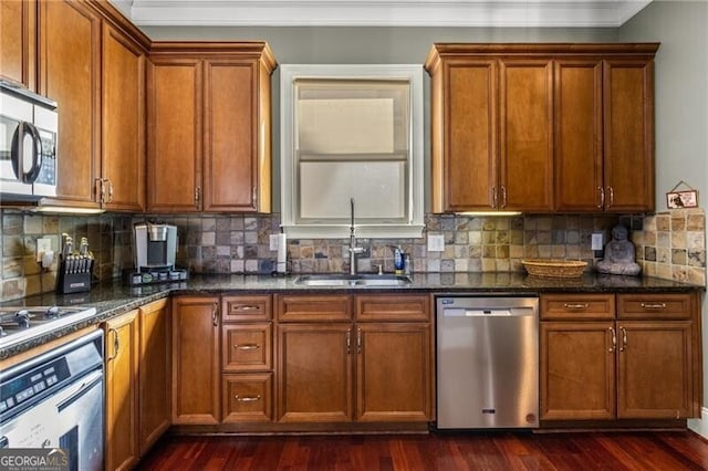 kitchen with a sink, backsplash, appliances with stainless steel finishes, brown cabinetry, and dark wood-style flooring