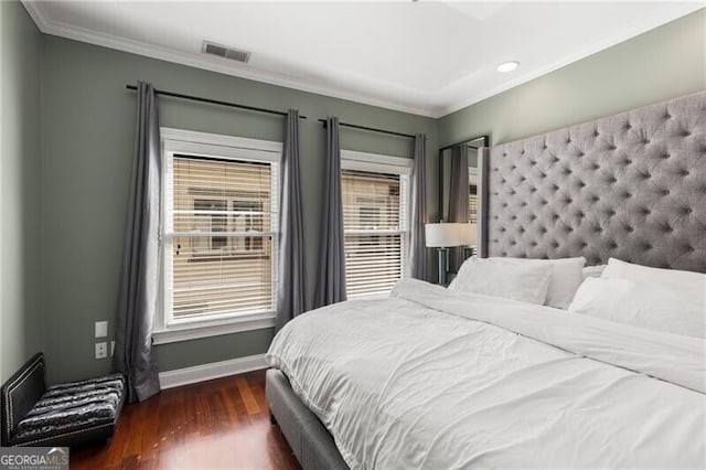 bedroom featuring baseboards, wood finished floors, visible vents, and ornamental molding