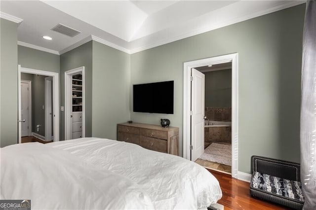 bedroom featuring visible vents, baseboards, ornamental molding, wood finished floors, and ensuite bath