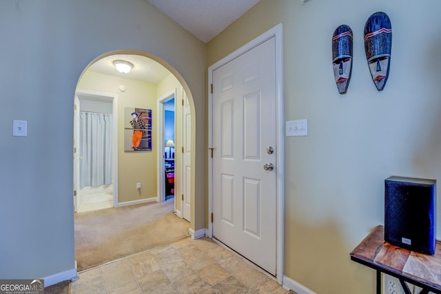 foyer entrance with arched walkways, light colored carpet, a textured ceiling, and baseboards