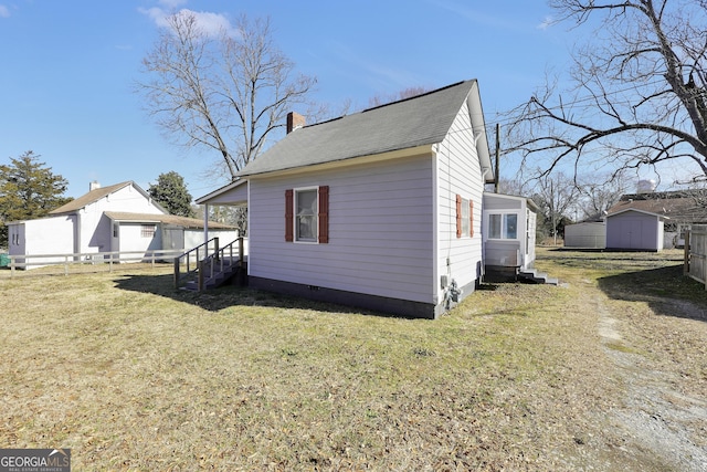 view of side of home featuring entry steps, fence, a storage shed, an outdoor structure, and a chimney