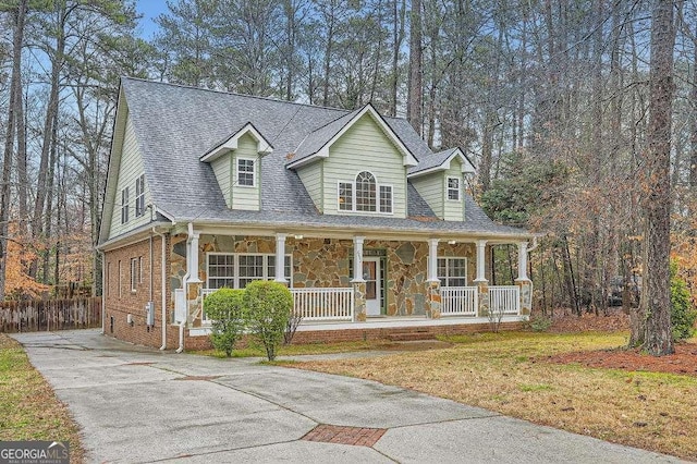 new england style home featuring driveway, covered porch, a shingled roof, stone siding, and brick siding