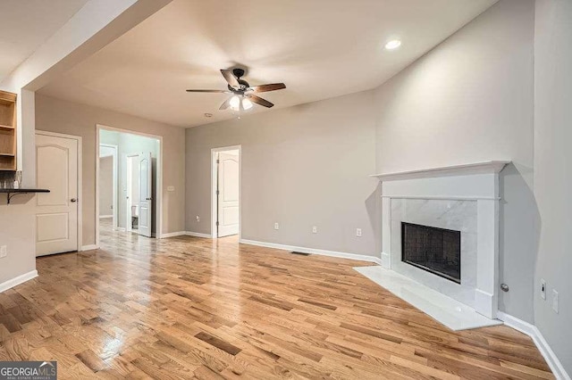 unfurnished living room with a high end fireplace, a ceiling fan, baseboards, and light wood finished floors