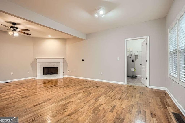 unfurnished living room featuring light wood finished floors, visible vents, baseboards, water heater, and a fireplace