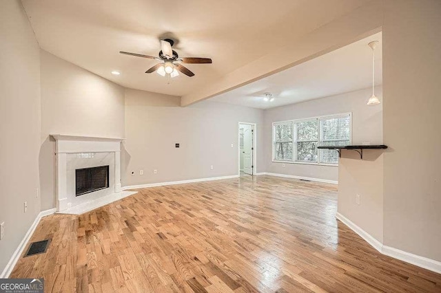 unfurnished living room featuring light wood finished floors, visible vents, ceiling fan, baseboards, and a premium fireplace