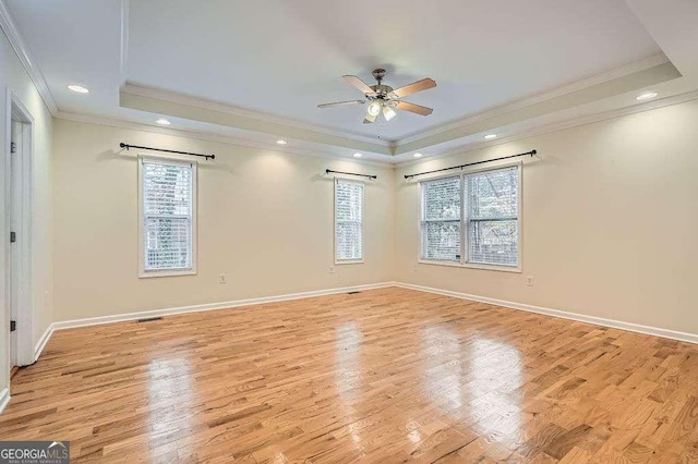 spare room with a tray ceiling, baseboards, and light wood-style flooring