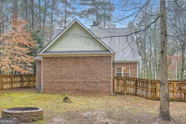 view of home's exterior with a chimney, a fire pit, brick siding, and fence