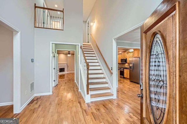 foyer entrance featuring visible vents, a high ceiling, a fireplace, stairs, and light wood-style floors