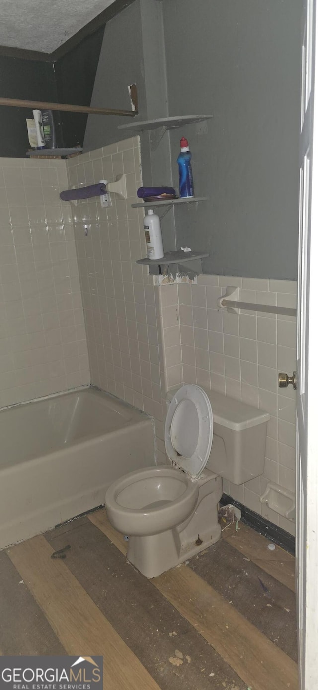 full bath with wood finished floors, bathtub / shower combination, wainscoting, tile walls, and toilet