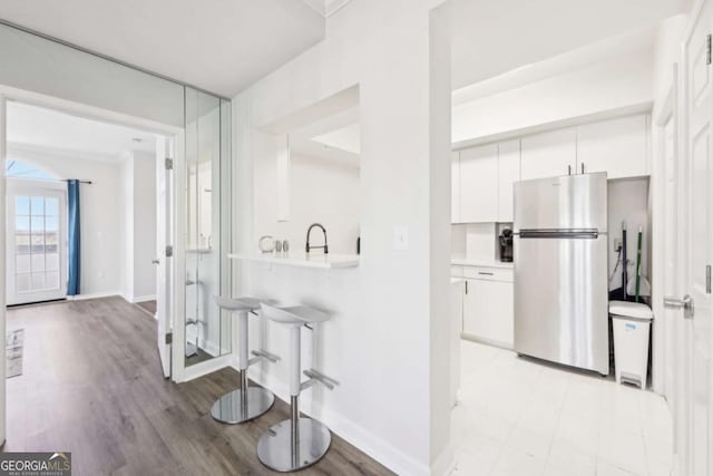 kitchen featuring light floors, a breakfast bar, freestanding refrigerator, light countertops, and white cabinetry