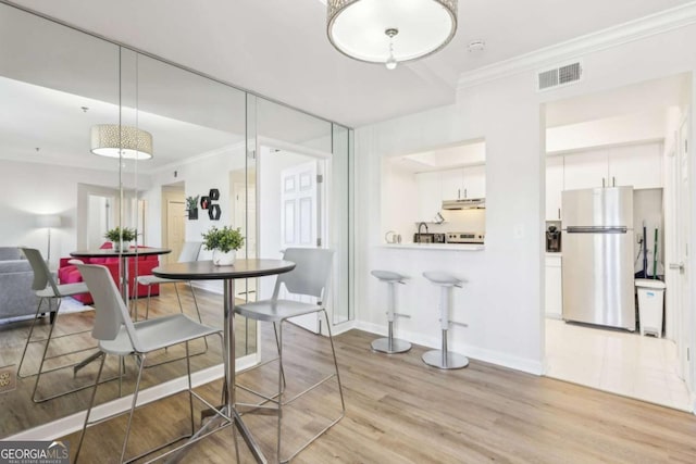 dining room featuring baseboards, visible vents, light wood finished floors, and ornamental molding