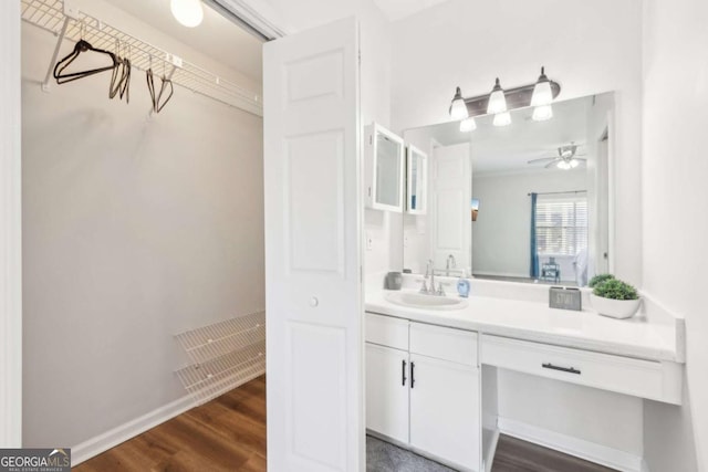 bathroom featuring a walk in closet, ceiling fan, baseboards, wood finished floors, and vanity