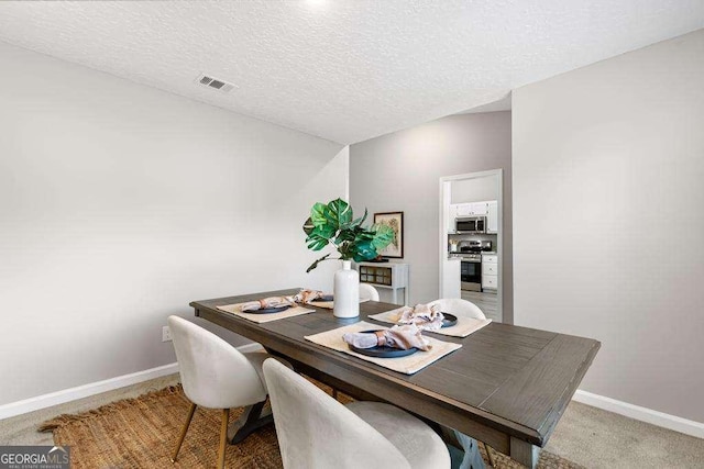 dining room with visible vents, light colored carpet, a textured ceiling, and baseboards