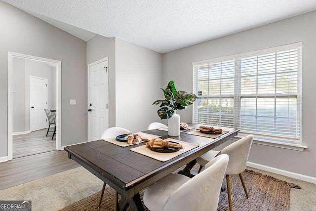 dining room with a textured ceiling, baseboards, and wood finished floors