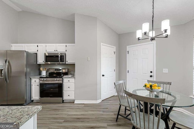 kitchen featuring decorative light fixtures, a textured ceiling, stainless steel appliances, white cabinets, and light wood finished floors