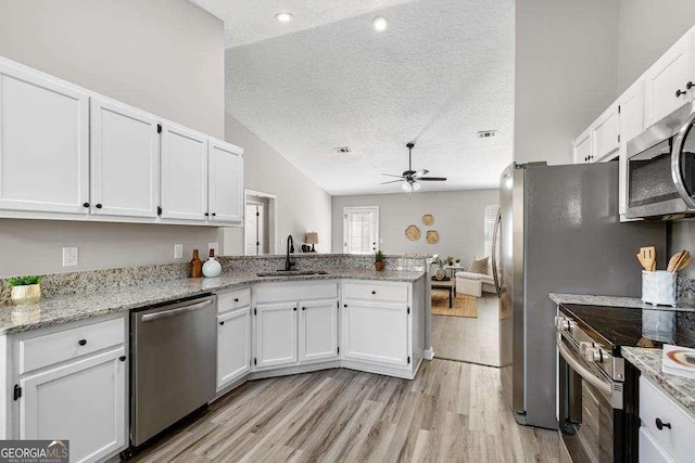 kitchen featuring a peninsula, a sink, appliances with stainless steel finishes, a textured ceiling, and white cabinetry