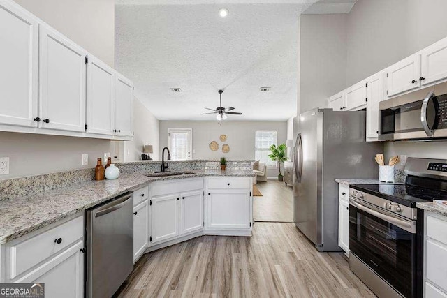 kitchen with a sink, a textured ceiling, white cabinetry, appliances with stainless steel finishes, and a peninsula