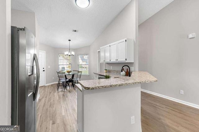 kitchen with visible vents, vaulted ceiling, a peninsula, stainless steel refrigerator with ice dispenser, and a sink